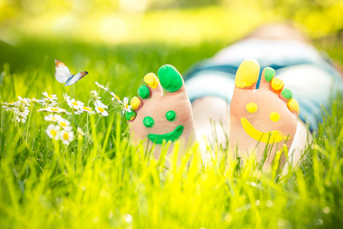 Child Lying on Green Grass with Smiley Faces Painted on Feet