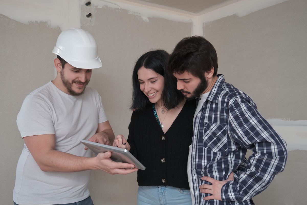 Contractor showing plans on a tablet to a couple inside a home under construction.